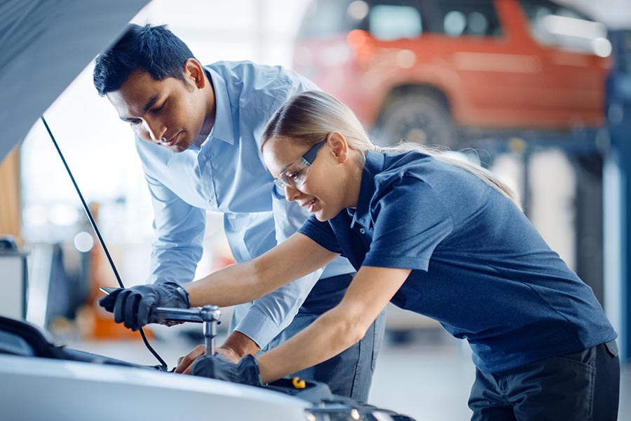 Business Insurance - Two Auto Mechanics Collaborate over a Vehicle, Wearing Safety Gear